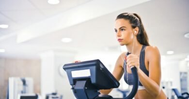 Serious fit woman in earphones and activewear listening to music and running on treadmill in light contemporary sports center