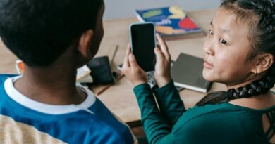 From above of adorable little Asian girl showing mobile phone to unrecognizable African American boy during break in classroom