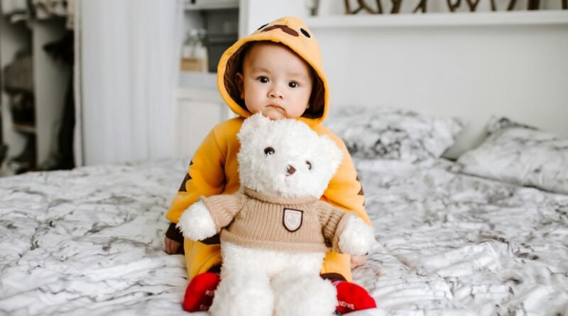 toddler sitting on bed beside white bear plush toy