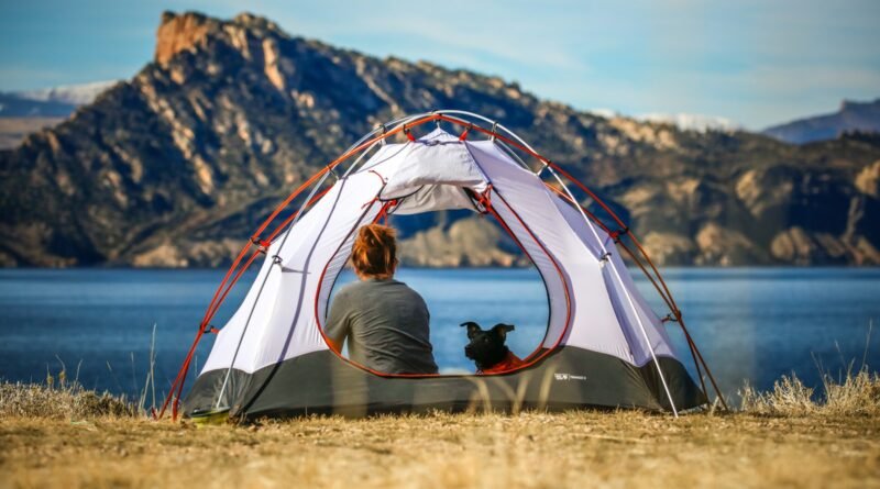 woman and a dog inside outdoor tent near body of water